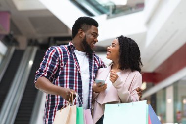 Alışveriş merkezinde alışveriş yaparken indirimli uygulama kullanan genç siyahi çift.