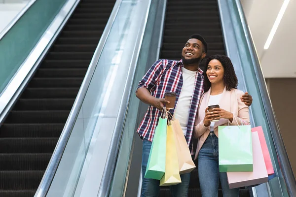 Alegre pareja negra montando escaleras mecánicas después de ir de compras en los grandes almacenes —  Fotos de Stock