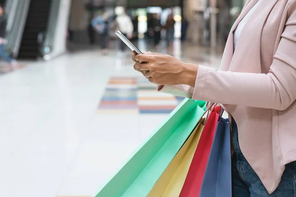 Shoppingapp. Svart kvinna bär Shopper väskor och använda smartphone i köpcentret — Stockfoto