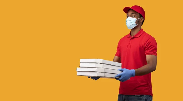 Repartidor negro con máscara y guantes sosteniendo cajas de pizza — Foto de Stock