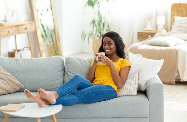 Full length πορτρέτο της χιλιετίας μαύρο γυναίκα ψύξη στον καναπέ με φλιτζάνι καφέ στο σπίτι, ελεύθερο χώρο — Φωτογραφία Αρχείου