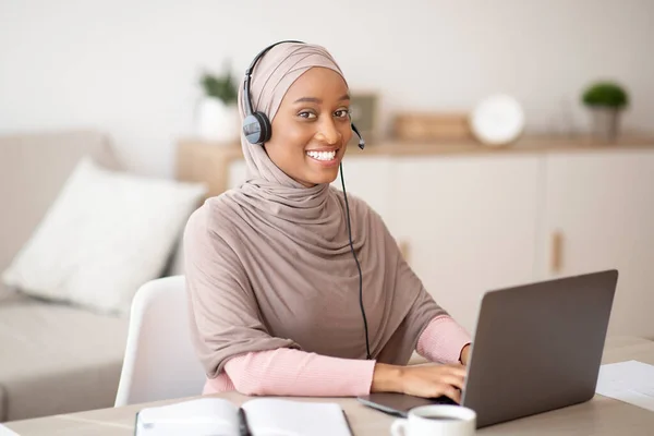 Reunião de negócios online. Mulher negra em hijab usando fones de ouvido e computador portátil para videoconferência em casa — Fotografia de Stock