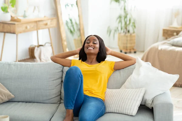 Χαρούμενη μαύρη γυναίκα χαλαρώνοντας σε άνετο καναπέ στο σπίτι, έχοντας ειρηνική ώρα το πρωί του Σαββατοκύριακου — Φωτογραφία Αρχείου