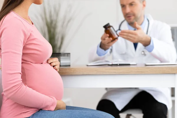 Mature experienced doctor showing pills to pregnant lady — Stock Photo, Image