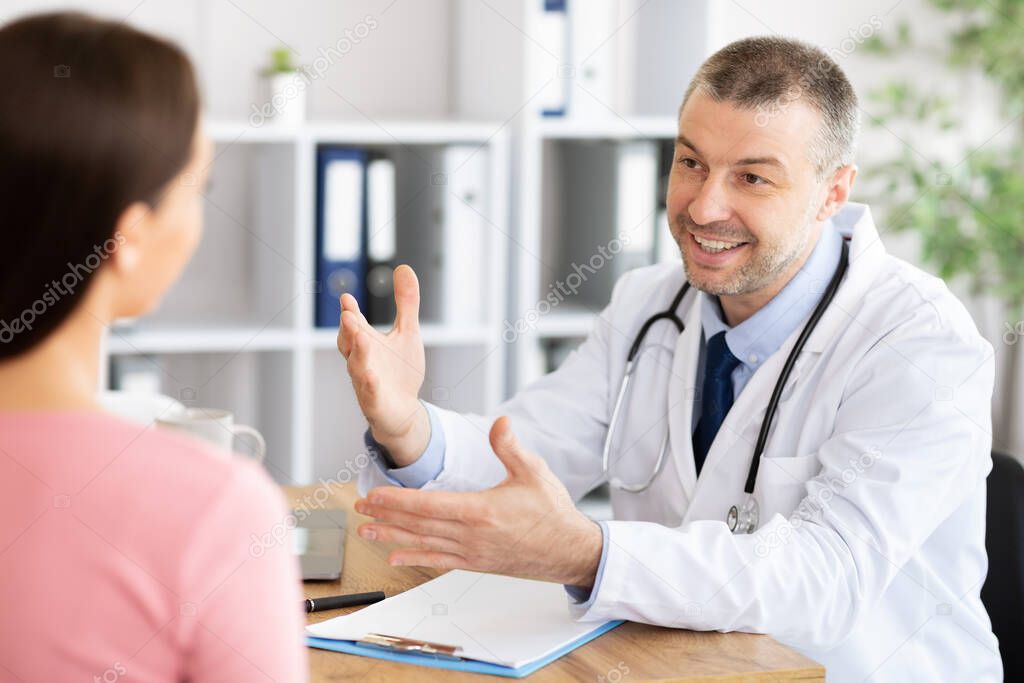 Middle aged smiling experienced doctor talking to his patient
