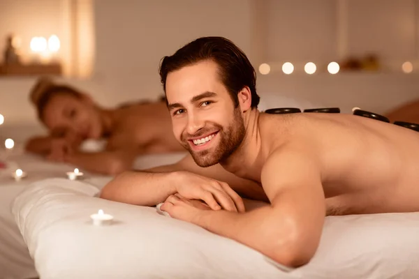 Feliz hombre relajante durante parejas caliente piedras masaje en spa — Foto de Stock