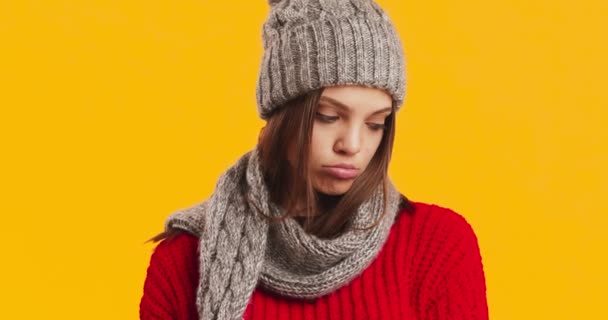 Close-up portret van trieste jonge vrouw dragen winter hoed en sjaal, pruilen lippen, oranje studio achtergrond — Stockvideo