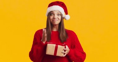 Noel Baba şapkalı mutlu bayan elinde Noel hediyesi ve gülüyor, şimdiki ve turuncu geçmişinin tadını çıkarıyor.