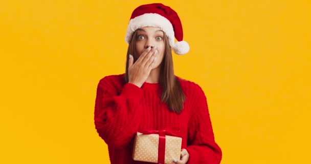 Studioaufnahme einer jungen glücklichen Frau mit Weihnachtsmütze in Geschenkbox und lächelndem, orangefarbenem Studiohintergrund — Stockvideo
