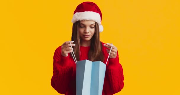 Έκπληκτη νεαρή γυναίκα σε Σάντα καπέλο κοιτάζοντας μέσα στην τσάντα αγορών, βρέθηκε τέλειο χριστουγεννιάτικο δώρο — Αρχείο Βίντεο