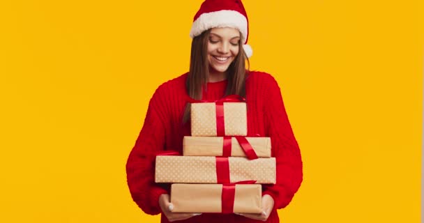 Mujer joven feliz en sombrero de Navidad sosteniendo un montón de cajas de regalo, fondo de estudio naranja — Vídeos de Stock