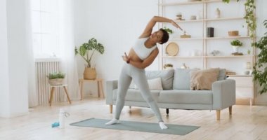 Genç yogi siyah bayan vücudunu yana doğru eğiyor, ağır çekimde.