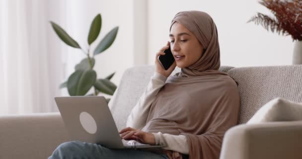 Remote work and freelance concept. Young muslim lady consulting client by phone, browsing on laptop — Stock Video