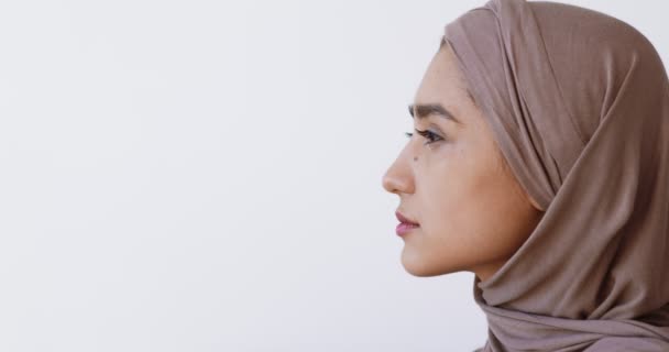 Nahaufnahme Porträt einer jungen muslimischen Dame im Hijab, die den Kopierraum betrachtet, weißer Studiohintergrund — Stockvideo