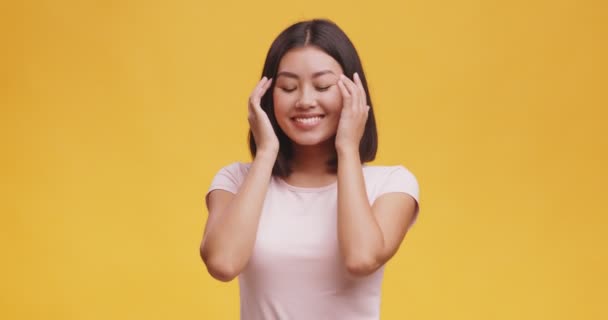 Studioporträt einer jungen niedlichen asiatischen Dame, die ihr Haar sträubt und in die Kamera lächelt, orangefarbener Hintergrund — Stockvideo