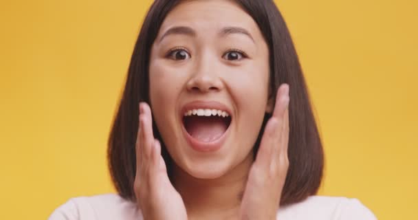 Close up of young amazed asian lady opening mouth and touching face in astonishment, yellow studio background — Stock Video