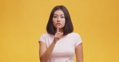 Sırrın işareti. Dudaklarında parmak tutan gizemli Asyalı kadın, turuncu stüdyo geçmişi..