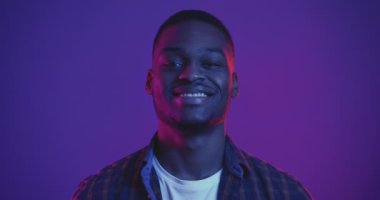 Neon ışıklarıyla kameraya gülümseyen Afrikalı Amerikalı genç adamın stüdyo portresi.