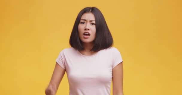 Angry asian woman pointing finger to camera, suspecting and blaming in lying, orange background — Stock Video