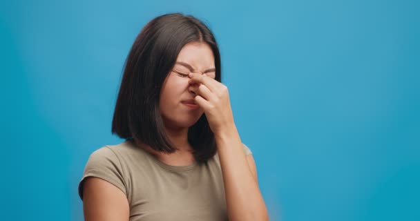 Gestresste jonge aziatische vrouw met verschrikkelijke hoofdpijn aanval, masseren neusbrug, blauwe studio achtergrond — Stockvideo