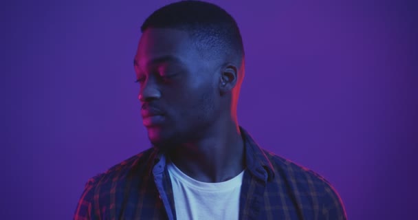 Profilo ritratto di un giovane afroamericano che si gira verso la macchina fotografica, guardando seriamente, girato in studio con luci al neon, — Video Stock