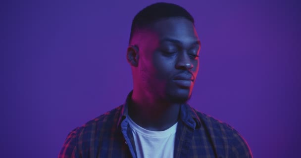 Närbild porträtt av allvarliga självsäker afrikansk amerikansk kille vända ansikte mot kamera och ser allvarligt i neon ljus — Stockvideo