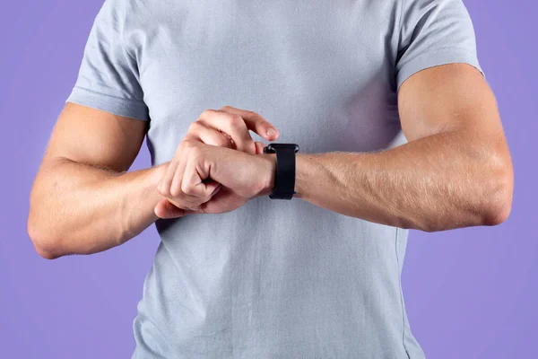 Unrecognizable young sportsman checking his smartwatch on violet studio background, closeup — Stock Photo, Image