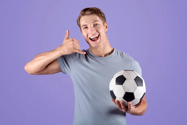 Steun uw favoriete speler of sportteam. gelukkig jonge kerel met voetbal maken CALL ME teken op violette achtergrond — Stockfoto