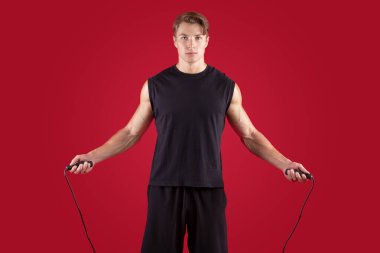 Aerobik konsepti. Kırmızı stüdyo arka planında ip atlayan ciddi bir atletizm sporcusu.