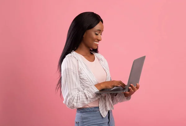 Millennial donna afroamericana che lavora con il computer portatile, lavorando o studiando online su sfondo rosa — Foto Stock
