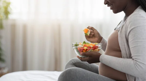 Чорна вагітна леді насолоджується свіжим овочевим салатом сидячи на ліжку — стокове фото