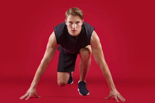 Full length portret van atletische jonge loper staan op start over rode studio achtergrond — Stockfoto