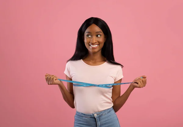 La pérdida de peso y el concepto de dieta saludable. Feliz dama afroamericana midiendo sus pechos sobre fondo de estudio rosa — Foto de Stock