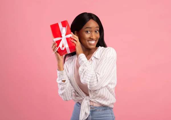 Jovem mulher negra segurando caixa de presente com fita, sentindo-se animado para celebrar férias no fundo do estúdio rosa — Fotografia de Stock