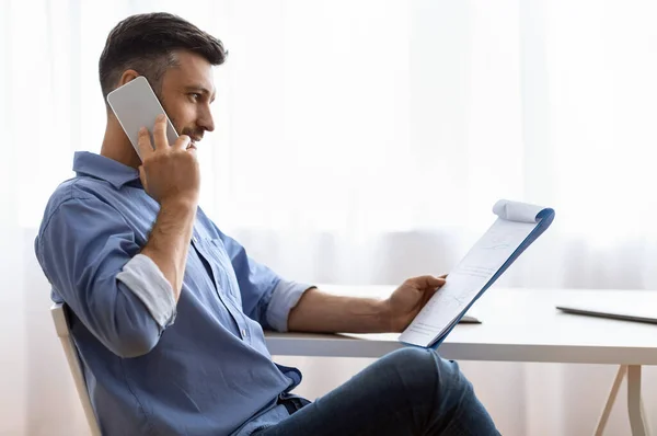Imprenditore maschio occupato che parla sul cellulare e che controlla i rapporti finanziari all'ufficio — Foto Stock