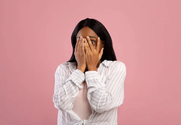 Porträtt av ung svart kvinna som täcker ansiktet med händer, känna sig rädd eller stressad på rosa studio bakgrund — Stockfoto
