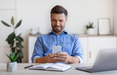 Ofiste dinlenirken akıllı telefondaki gülümseyen iş adamı mesajı.
