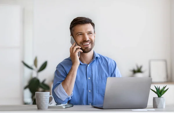 Empresario hablando en el teléfono celular mientras trabaja en el escritorio con el ordenador portátil en la oficina — Foto de Stock
