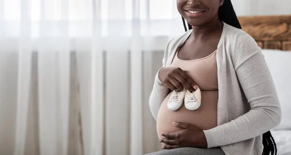 Bonne attente. Noir Expectant Femme tenant de petites chaussures de bébé près du ventre enceinte — Photo