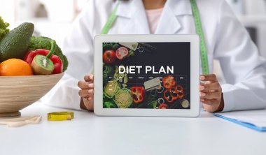 Siyahi diyetolog doktor bayan açık diyet uygulaması ile dijital tablet gösteriyor