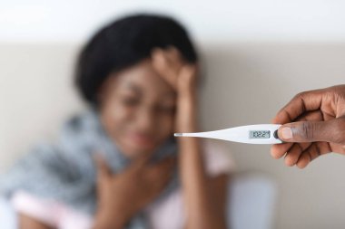 Ateşli siyah bir kadın, erkek eli termometre.