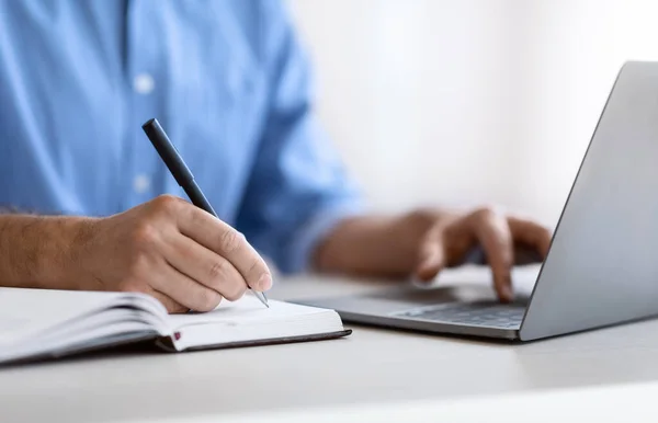 Onherkenbare man die in notitieblok schrijft en laptop op kantoor gebruikt, close-up — Stockfoto