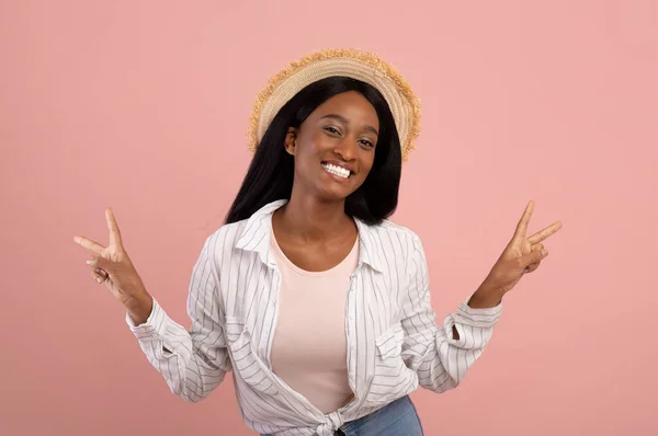 Pozitív fekete nő alkalmi ruhák és szalma kalap gesztikuláló béke rózsaszín stúdió háttér — Stock Fotó