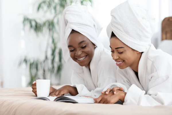 Sluiten van glimlachende zwarte dames liggend op bed, lectuur tijdschrift — Stockfoto