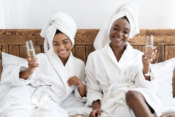 Duas lindas senhoras negras em roupões de banho bebendo champanhe — Fotografia de Stock