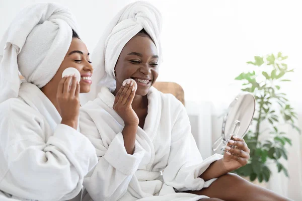 Afro-Amerikaanse vrouwelijke vrienden in badjassen reinigen gezichten thuis — Stockfoto