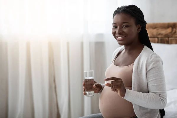 Vitaminer från födseln. Gravid svart kvinna som håller tillägg piller och glas vatten — Stockfoto