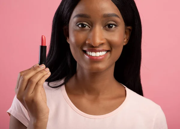 Linda mulher negra segurando tubo de batom no fundo do estúdio rosa — Fotografia de Stock