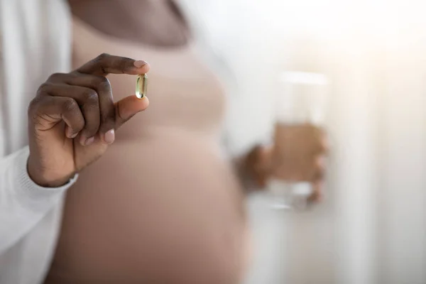 Graviditetstillskott. Svart gravid dam som håller vitamin kapsel och glas vatten — Stockfoto