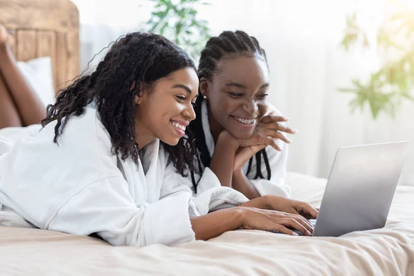 Glada svarta kvinnor i badrockar med laptop hemma, websurfing — Stockfoto